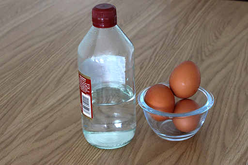 An image of three eggs in a bowl next to a bottle of vinegar.