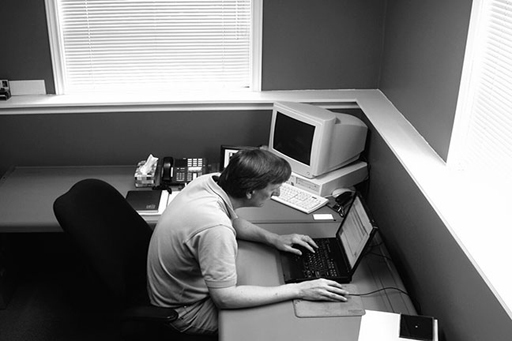 This is a photograph of a man at a desk using a laptop.