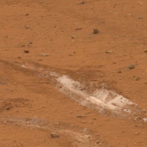 This figure is a photograph taken by the Spirit rover of the martian surface. The surface is coloured orange, and is fine grained with some larger pebbles. Across the centre of the image are two small valleys in the soil, the interior of which are coloured white.