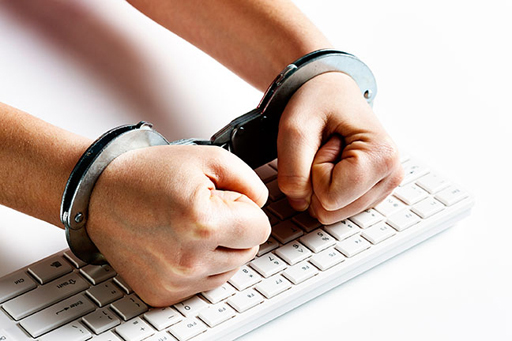 An image of a person's hands in handcuffs. Their clenched fists rest on a computer keyboard.