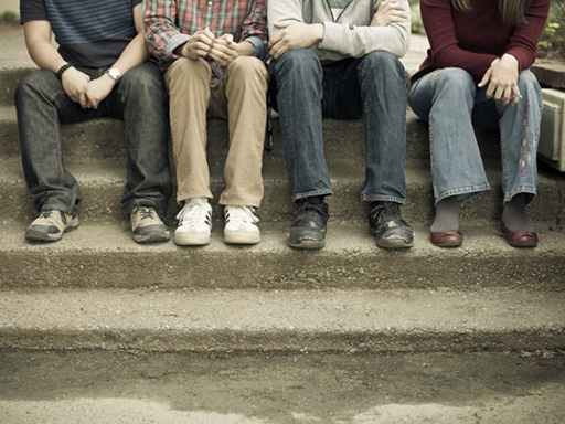 An image of four people sitting next to each other on a concrete step.