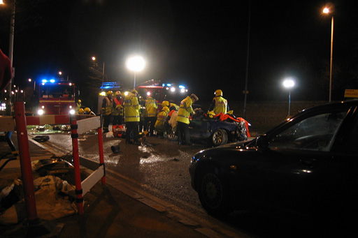 The scene of a serious road traffic accident at night, with attending emergency personnel wearing high visibility jackets.