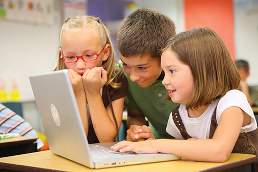 A photograph of three children using a laptop.