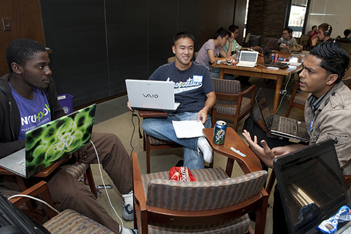 A photograph of three young men sat together each with laptops, engaging in a conversation.