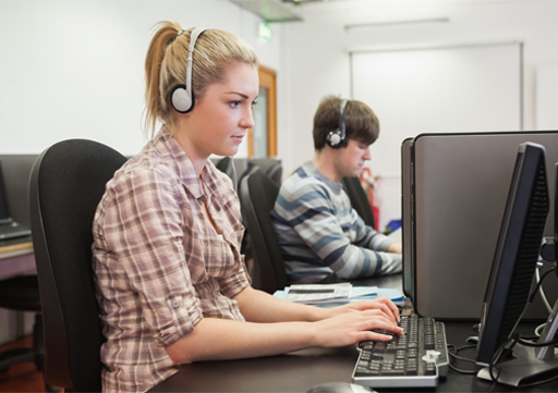 An image of two students at computers with headphones on.
