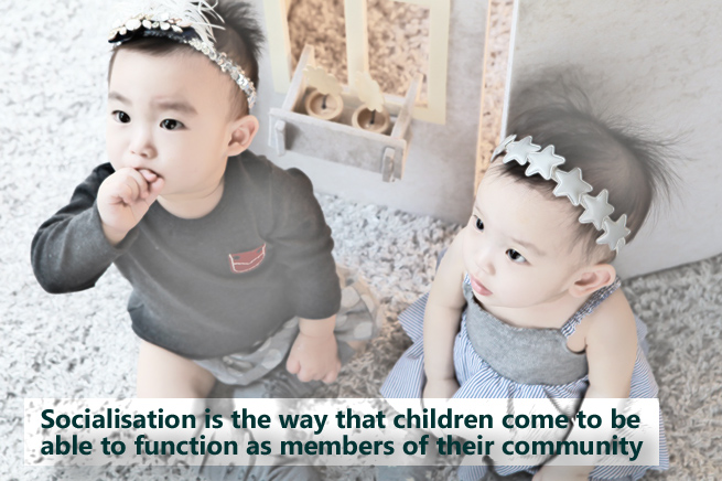 Two babies looking up with text 'Socialisation is the way that children come to be able to function as members of their community'