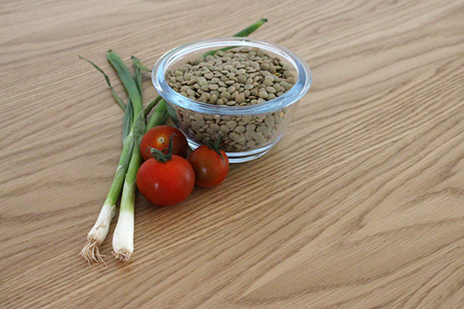 An image of a bowl of lentils on a table with spring onions and tomatoes.