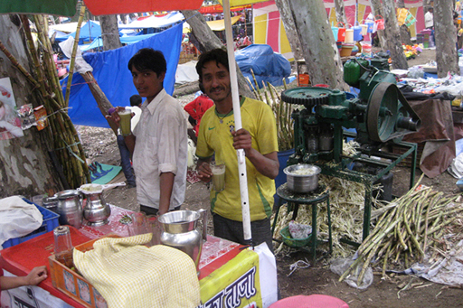 An image of two men at a roadside fair stall in India selling sugar cane juice in cups.