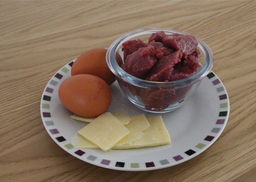 A photo of a small bowl of meet (beef) two eggs and a few slices of cheese.