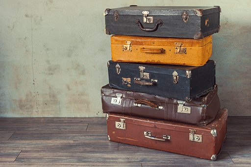 A stack of 5 old suitcases sitting on a wooden floor.