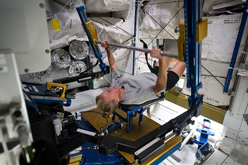 A colour photograph of an astronaut performing weightlifting on the ISS using an ARED.
