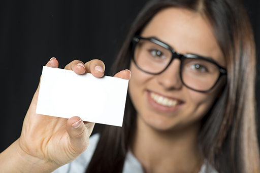 A smiling woman wearing glasses holds an empty business card.