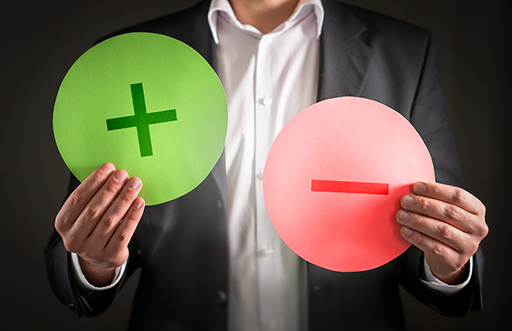 A person holds a green circle with a plus sign and a red circle with a minus sign.