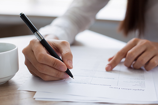 We see a person’s hand holding a pen, poised to begin filling out an application form.