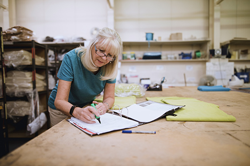 A woman in a workplace setting looks at ring binder and uses a pen to highlight key points.