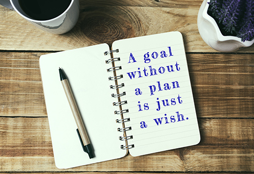 The phrase ‘A goal without a plan is just a wish’ is written on the open page of a small notebook.