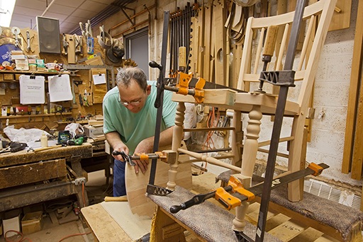 Photograph of man in a workshop carving wood to make a chair.