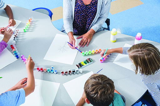 A photograph of a woman and a group of children painting.