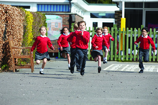 A photograph of a group of school children running in the playground.