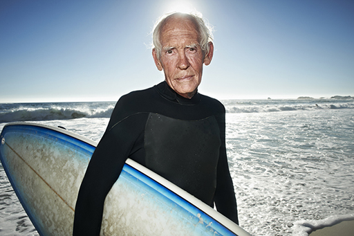 An image of an older man holding a surf board on a beach