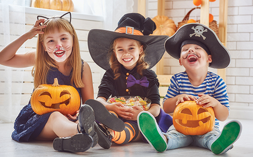 A photo showing three children in Halloween outfits holding sweets.