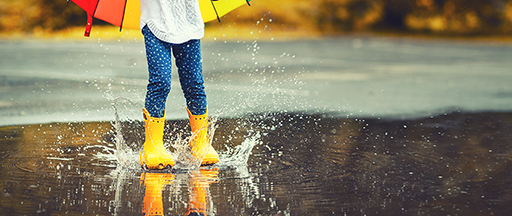 A photo of a child wearing wellies splashing in a puddle.