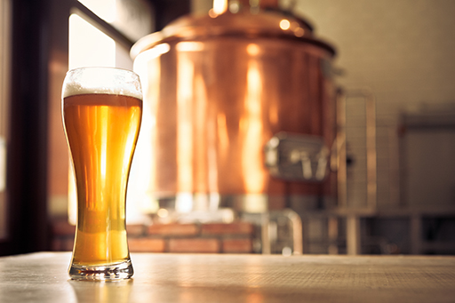 This is an image of a pint of beer in front of brewing equipment.