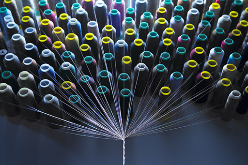 An image of many thread spools with threads drawn together below and twisted into one