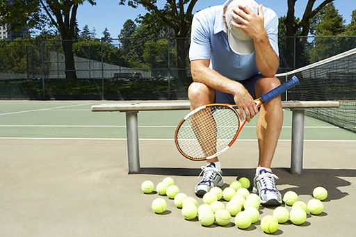 A man sits on a bench with his back to an empty tennis court.