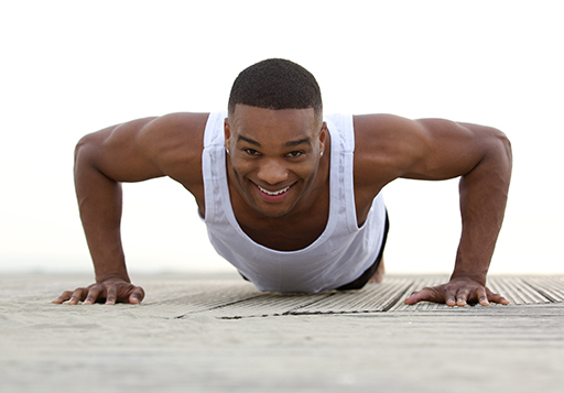 A man in a white gym vest is doing push ups on a wooden deck.