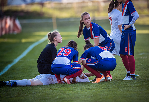 A group of female football players are gathered around an injured player who is lying on the pitch.