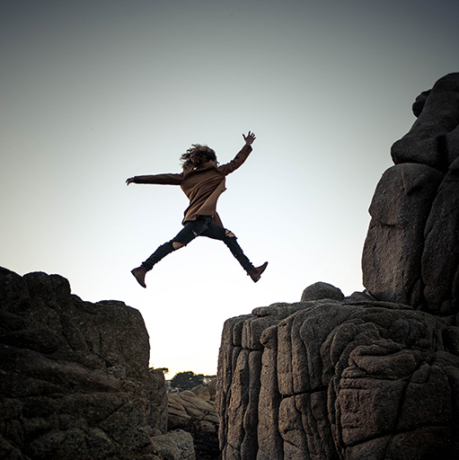 An image of a woman jumping from one large rock to another.