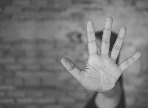 A black and white photo of a person’s palm held up and blocking their face.