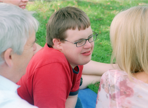 The image shows a young man with Down Syndrome sitting in between his parents.