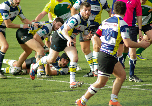 A photo of a Rugby game in which the central figure runs in to prepare to take a catch.