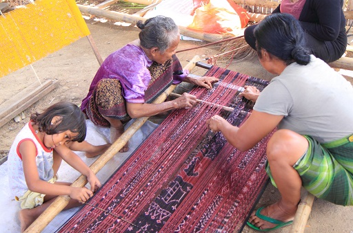 A photograph showing two adults and a child working on a woven piece of fabric.