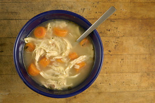 Bowl of chicken soup with a spoon resting against the side of the bowl.
