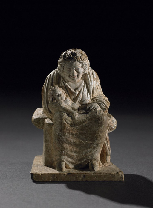 Terracotta figure of an old nurse sitting on a chair with a baby in her lap.