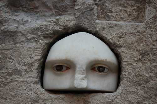 Stone carving showing the upper part of a female face with inlaid eyes, set into a wall.