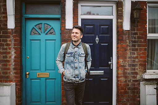This is a photograph of a man standing outside a front door.