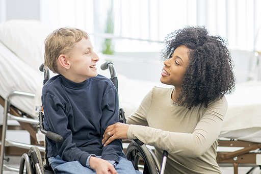 This is a photograph of a young woman interacting with a boy who is in a wheelchair.