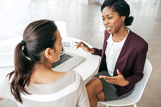 The figure is a photo of a female financial adviser talking to a young female client. They are both sitting around a table and the adviser has a lap top open in front of her.