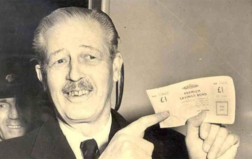 The image is a photograph of Harold Macmillan, Chancellor of the Exchequer in the 1950s and subsequently Prime Minister, holding a £1 Premium Bond.