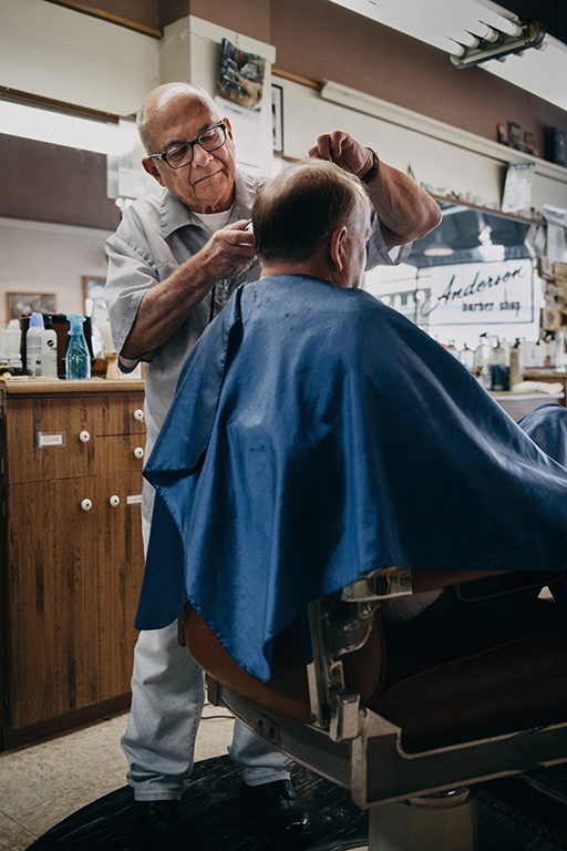 The figure is a photo of an older man having his hair cut in a barber’s shop.