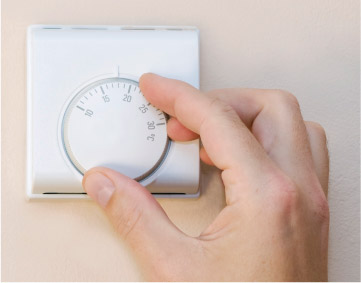 This photograph shows a hand moving the dial on a central heating thermostat.