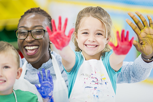 This is a photograph of a woman with two young children. They are painting and are showing the paint on their hands.