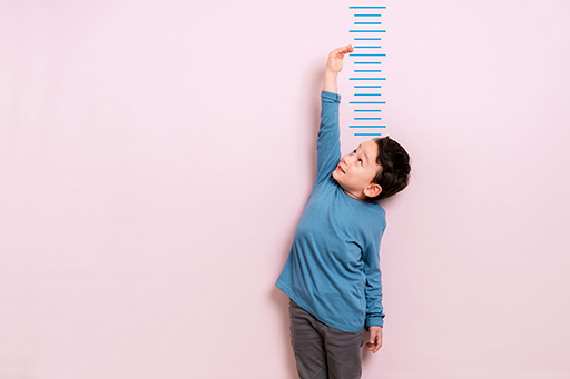 This is a photograph of a boy standing by a height chart.
