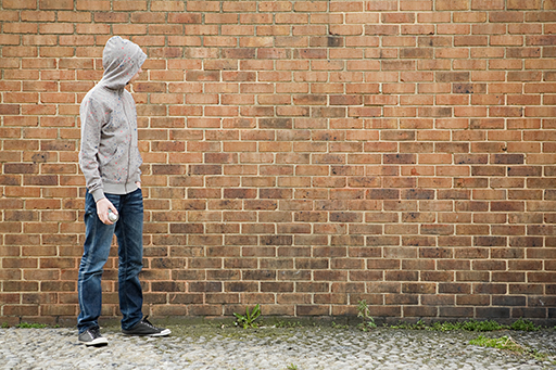This is a photograph of a young man standing next to a brick wall.