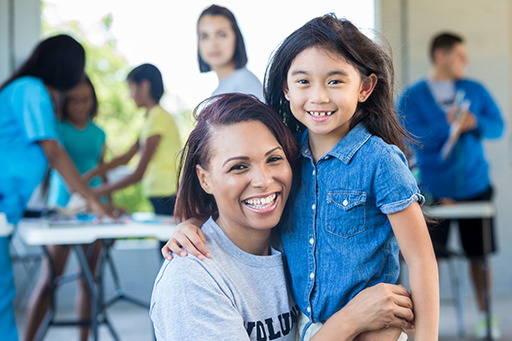 This is a photograph of a woman with a young child. There are more adults and children in the background.