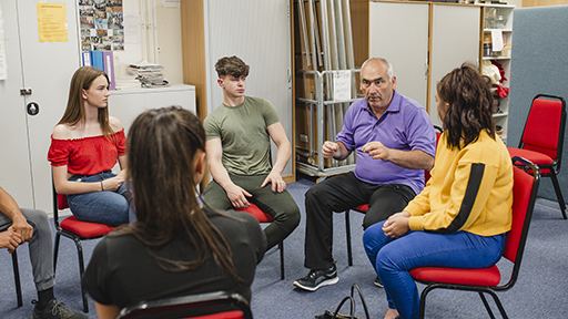 This is a photograph of a man with a group of young people. They are sitting in a circle.